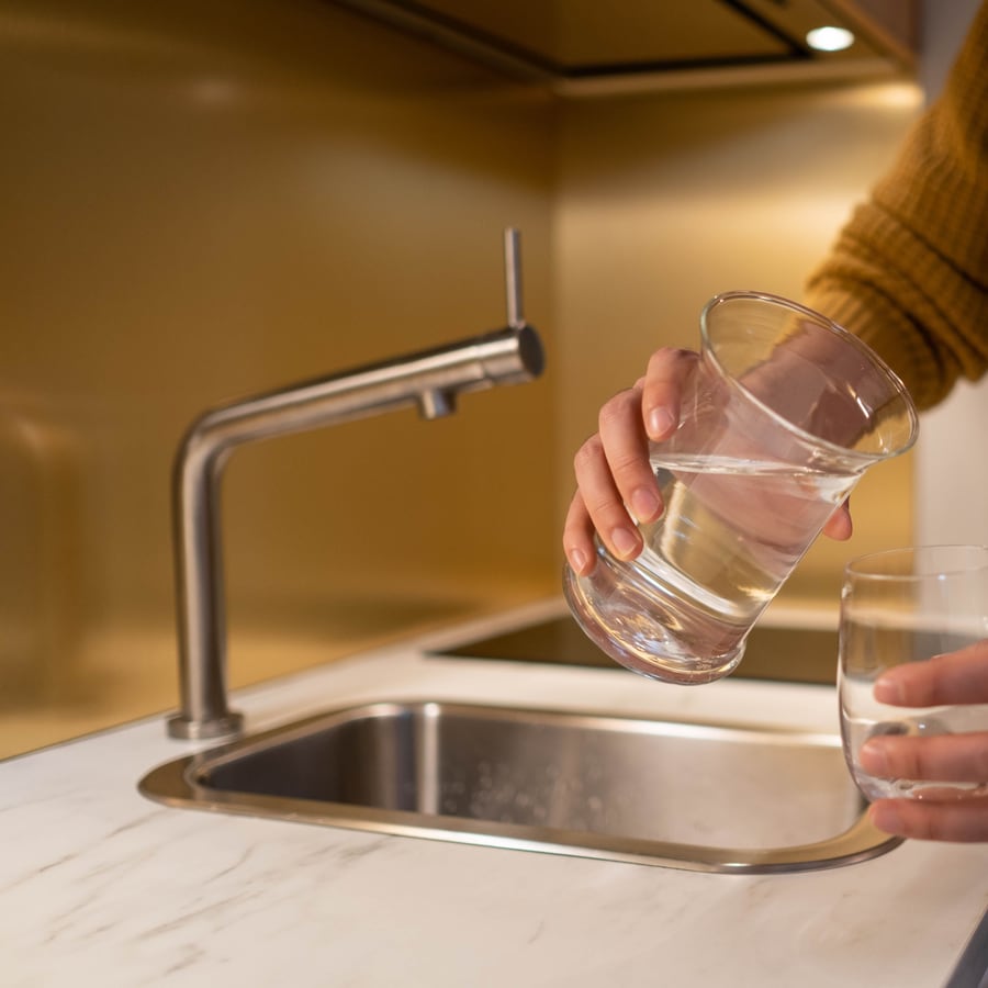 Glas wird an der Küchenarmatur gefüllt, die der Anlagenmechaniker angeschlossen hat