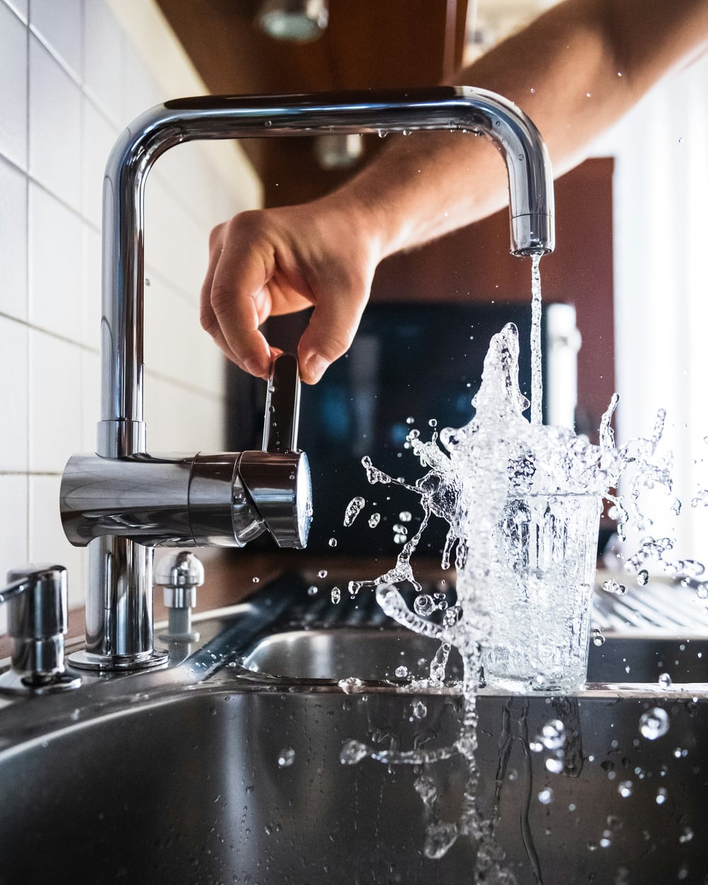 Glas unter einem laufenden Wasserhahn, den der Anlagenmechaniker in einer modernen Küche angeschlossen hat