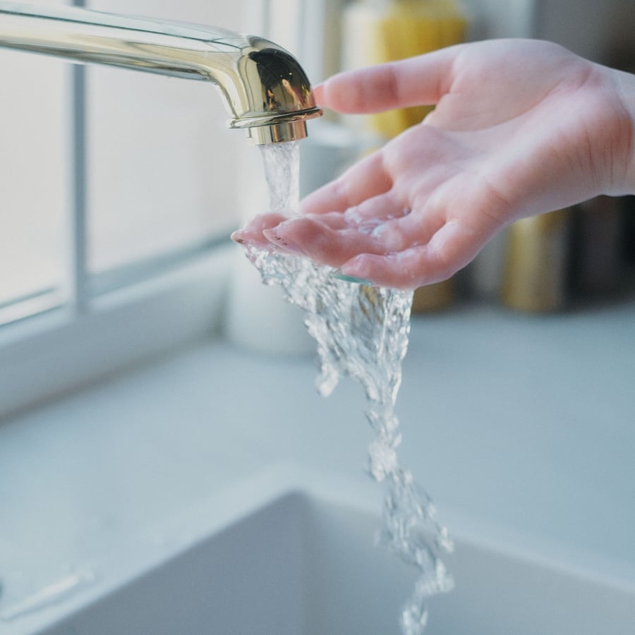 Hand unter fließendem Wasser an einer vom Anlagenmechaniker montierten Armatur über einem Spülbecken